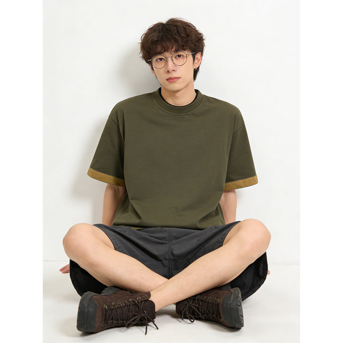 Seated model wearing an olive short-sleeve crew-neck T-shirt with tan sleeve-cuff trim.