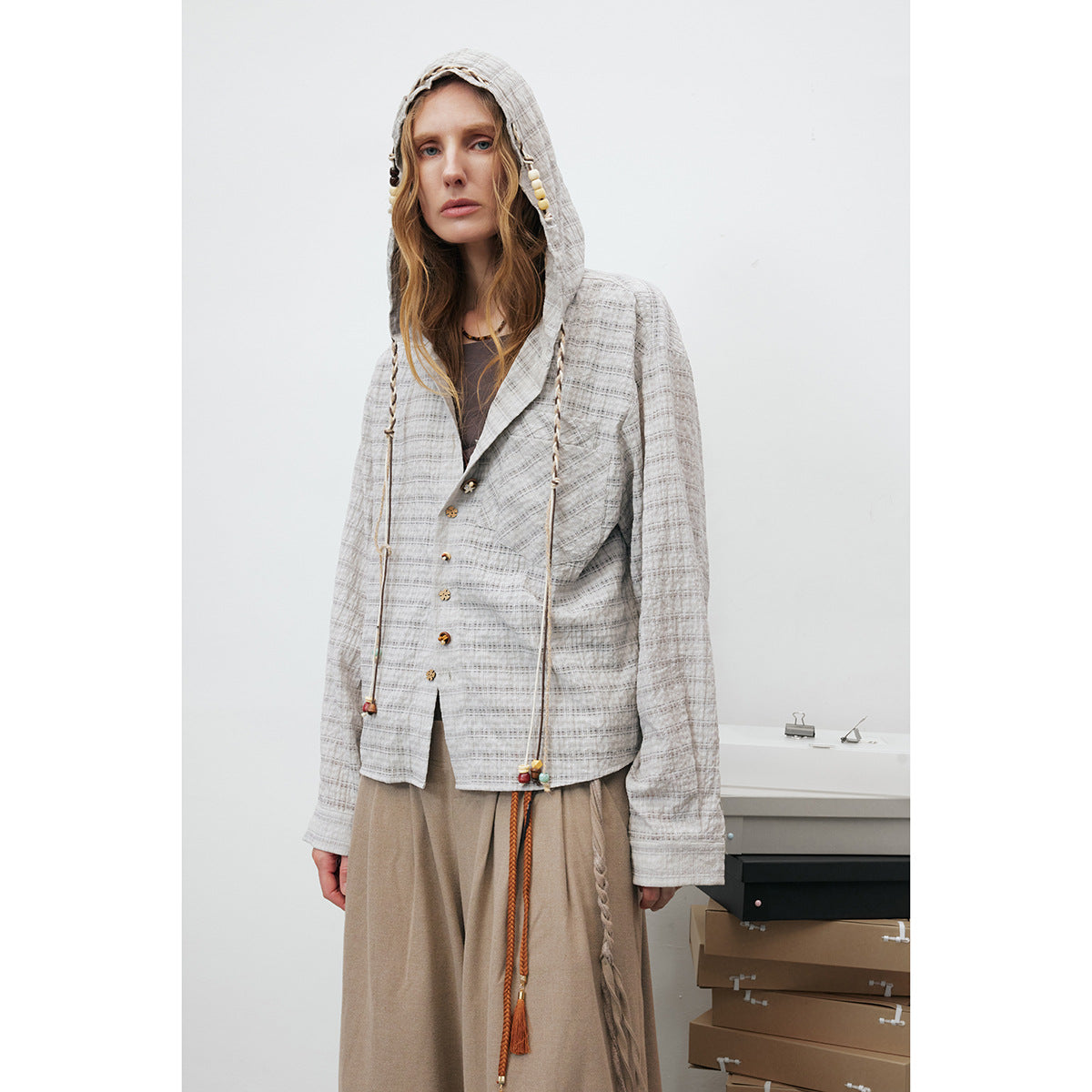 Model wearing a light gray plaid hooded jacket with braided drawstrings and decorative beads.