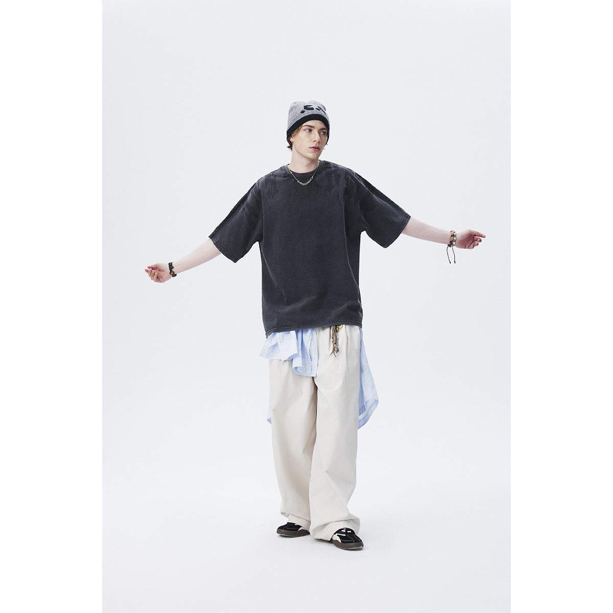 Model wearing a charcoal oversized T-shirt with subtle dark shoulder print and loose white trousers.