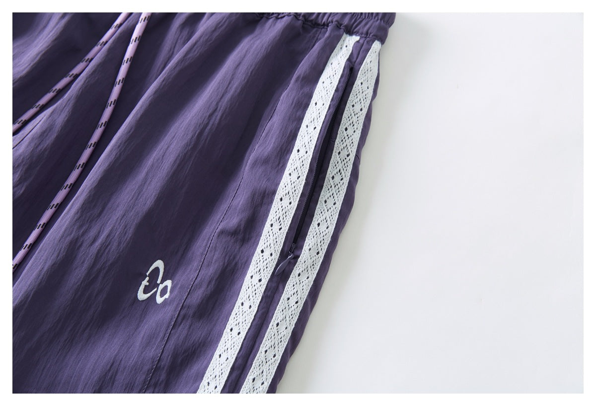 Close-up of purple pants showing the gathered waistband, drawcord, side zipper, and twin white lace stripes.