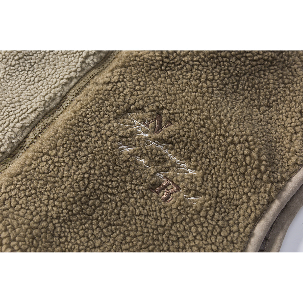 Close-up of khaki textured fleece with embroidered lettering and a small emblem.