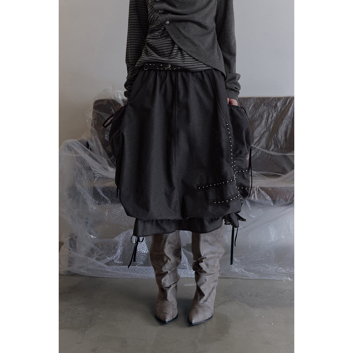 Close view of a charcoal gathered skirt with side ties, studded trim, and a ruffled hem, worn with a striped top.