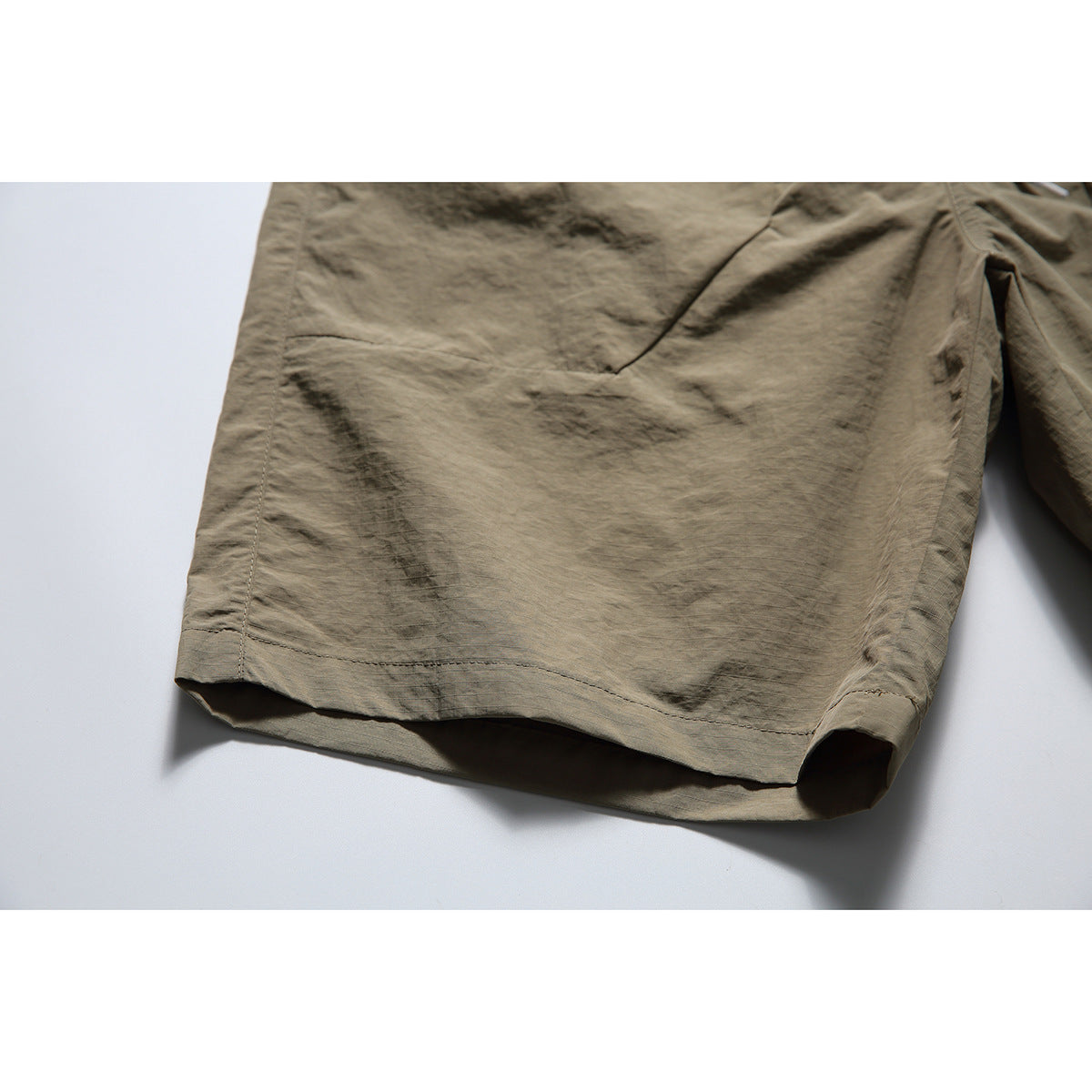 Close-up of the stitched hem and leg opening of taupe shorts.