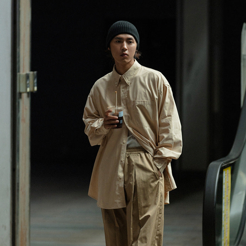 Model wearing an oversized beige button-up shirt and tan trousers with a black knit beanie.