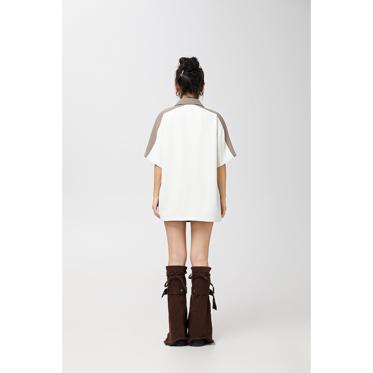 Back view of a model wearing an oversized white short-sleeve shirt with taupe collar and shoulder panels.