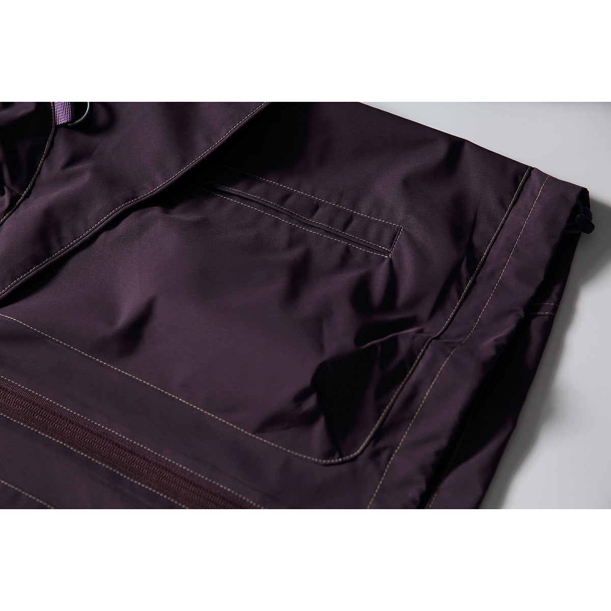 Close-up of a dark plum jacket's large pocket, zipper and contrast-stitched panels.