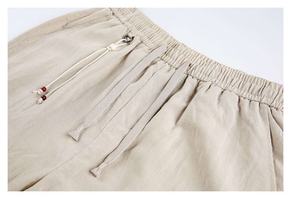 Close-up of beige pants showing the elastic waistband, drawstrings, and front pocket seams.