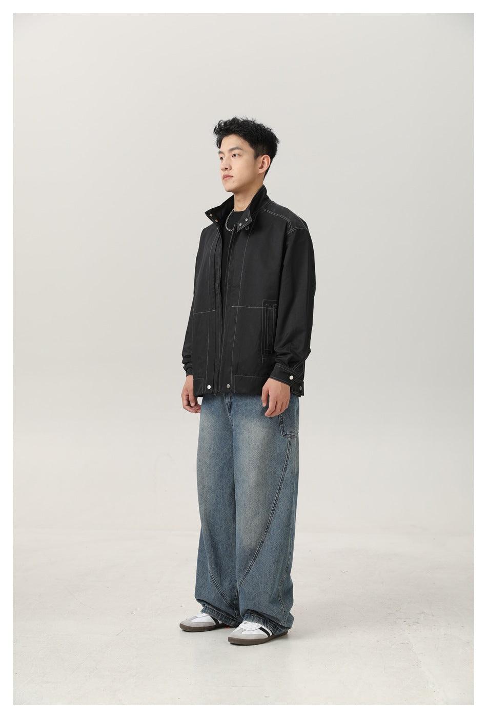 Man wearing black stand-collar jacket with contrast stitching, three-quarter side view, with wide-leg jeans