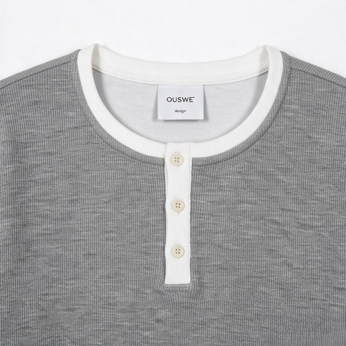 Close-up of a gray ribbed top with a white crew neckline, three-button placket, and visible sewn neck label.