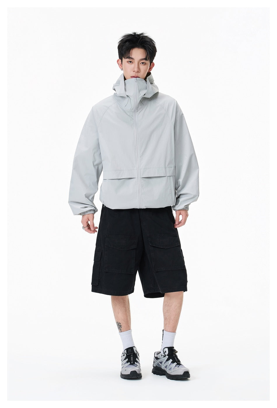 Full-length model wearing a light gray hooded zip jacket, black cargo shorts, white socks, and sneakers.