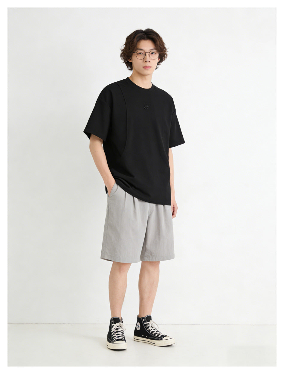 Model wearing a black oversized T-shirt with a small chest emblem and light gray shorts, shown from the front.
