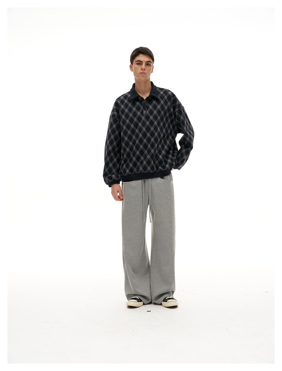Full-length model wearing a navy and gray diamond-plaid pullover with dark ribbed trim and gray wide-leg pants.