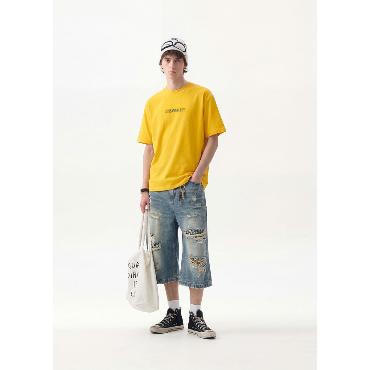 Full-length front view of a model in a yellow graphic T-shirt and distressed denim shorts.