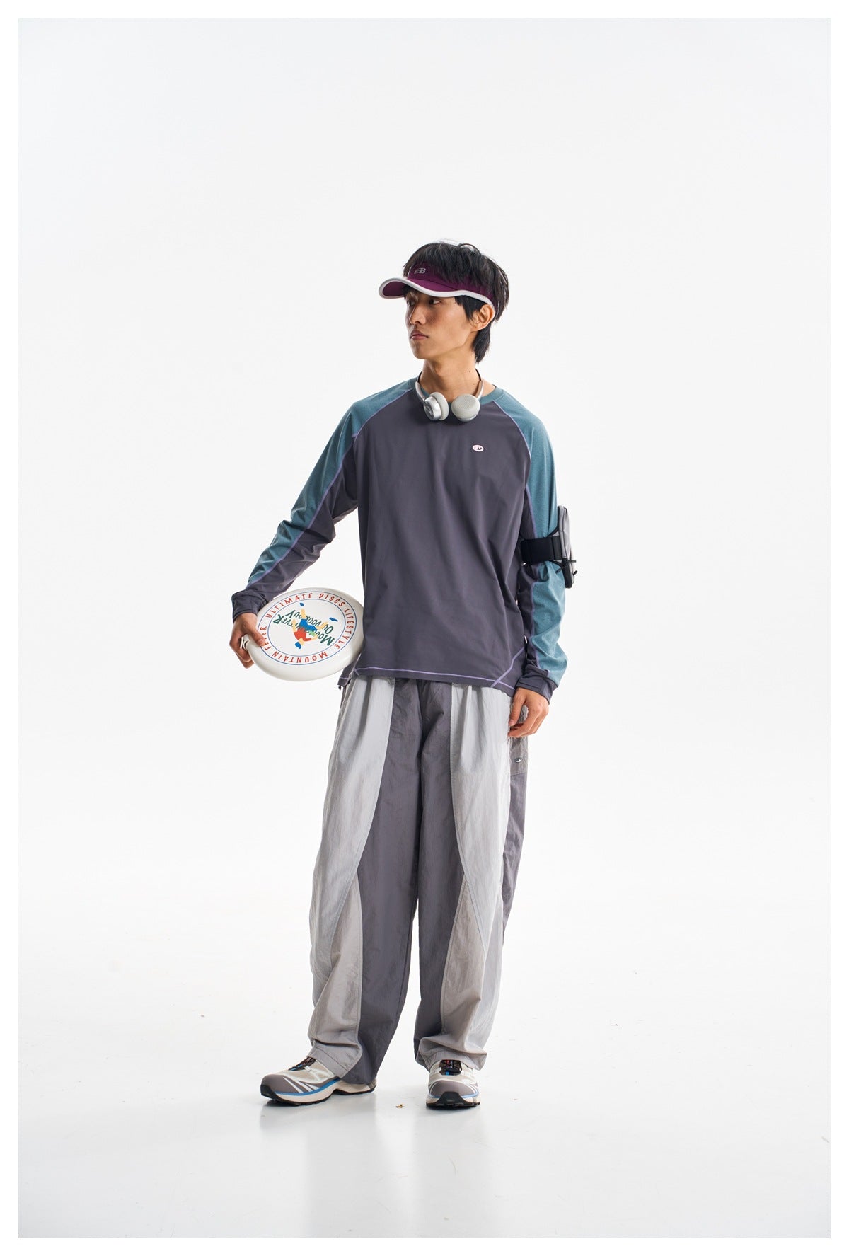 Model wearing a charcoal raglan shirt with teal sleeves and loose two-tone gray pants.