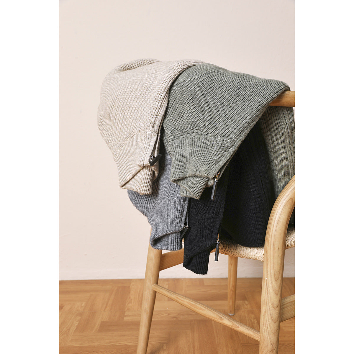 Rib-knit zip cardigans in cream, sage, gray, and black draped over a wooden chair.