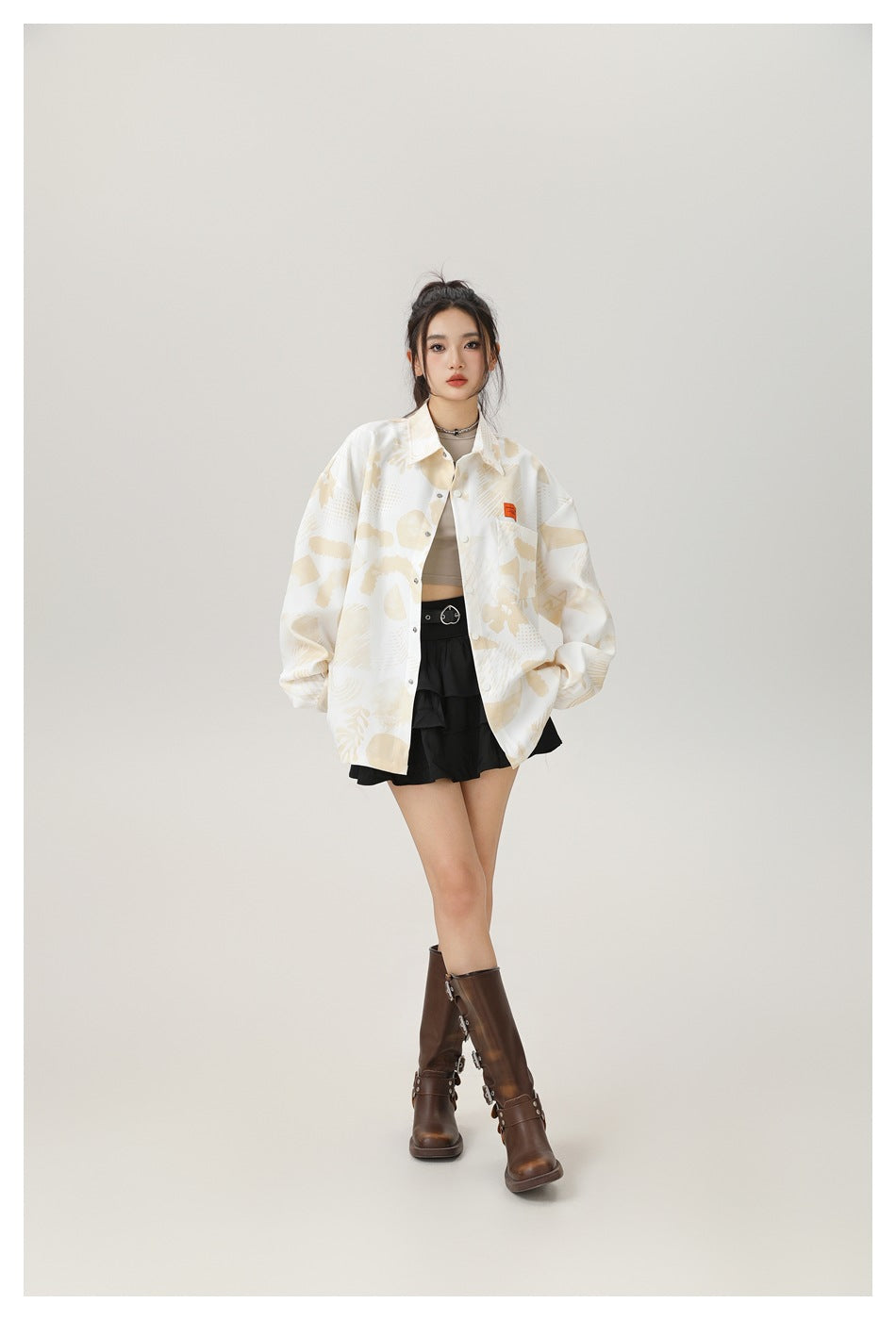 Model wearing an oversized cream shirt jacket with pale beige abstract print, layered over a crop top and black skirt.