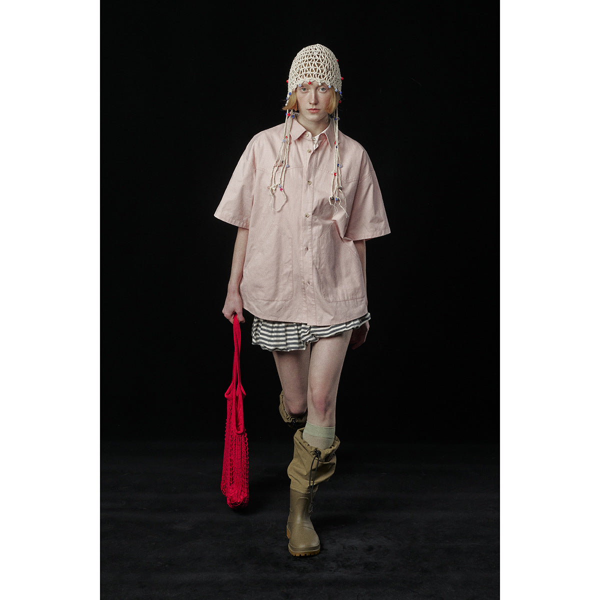Model wearing an oversized pale pink short-sleeve button-up shirt with large front pockets and striped shorts.