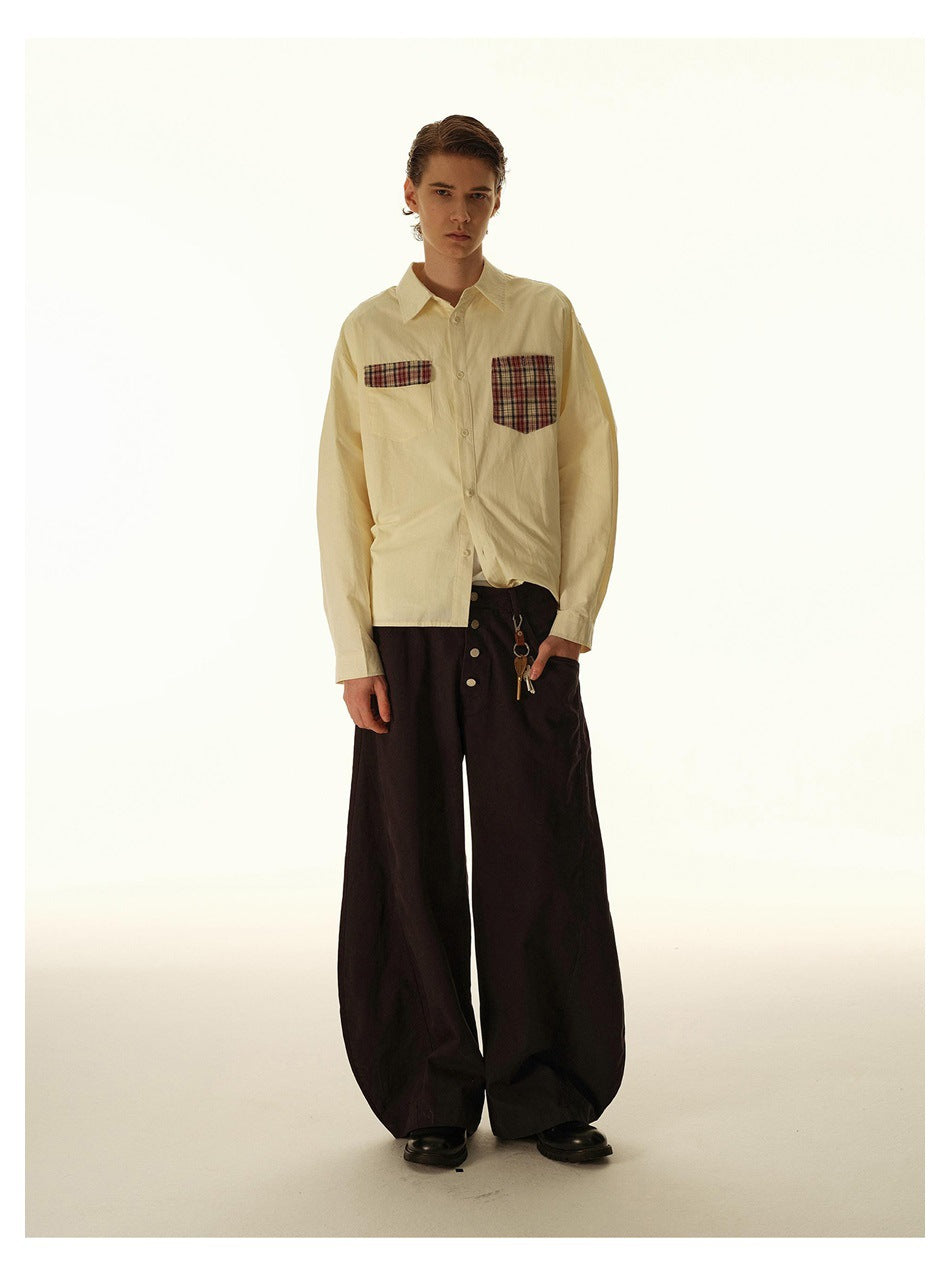 Full-length model wearing a cream button-up shirt with plaid chest pockets and wide dark trousers.