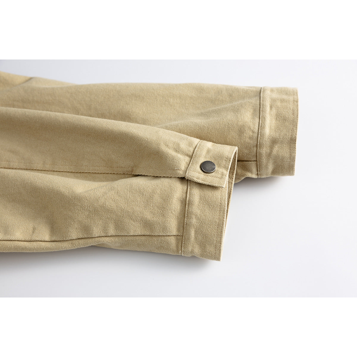 Close-up of a sand-colored jacket sleeve showing a cuff tab and dark snap.