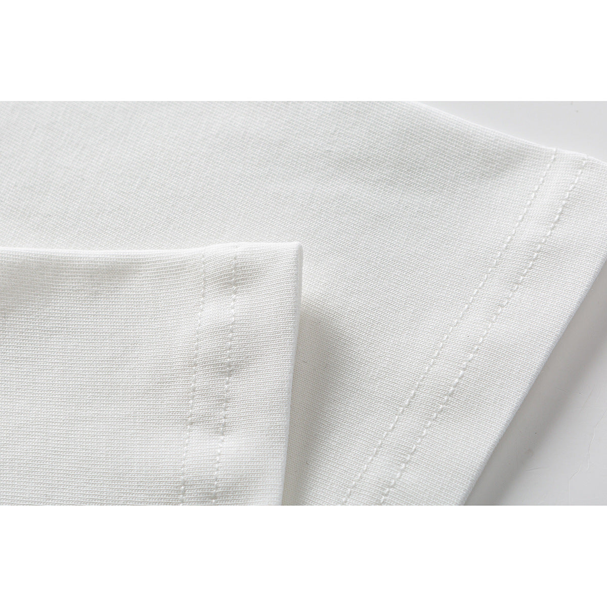 Close-up of white T-shirt fabric and double-stitched sleeve and hem edges.