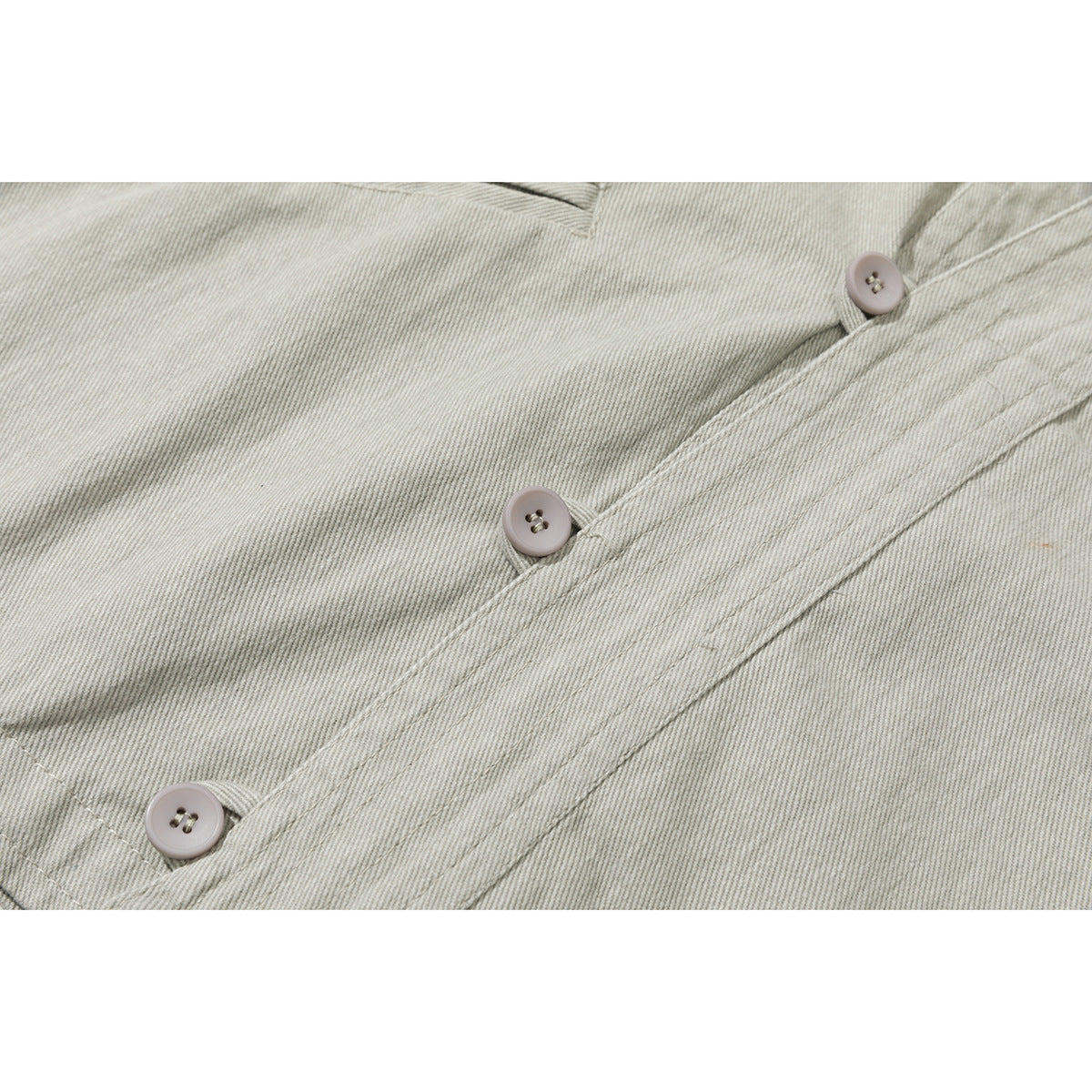 Close-up of three pale buttons and stitched placket on a light gray-green jacket.