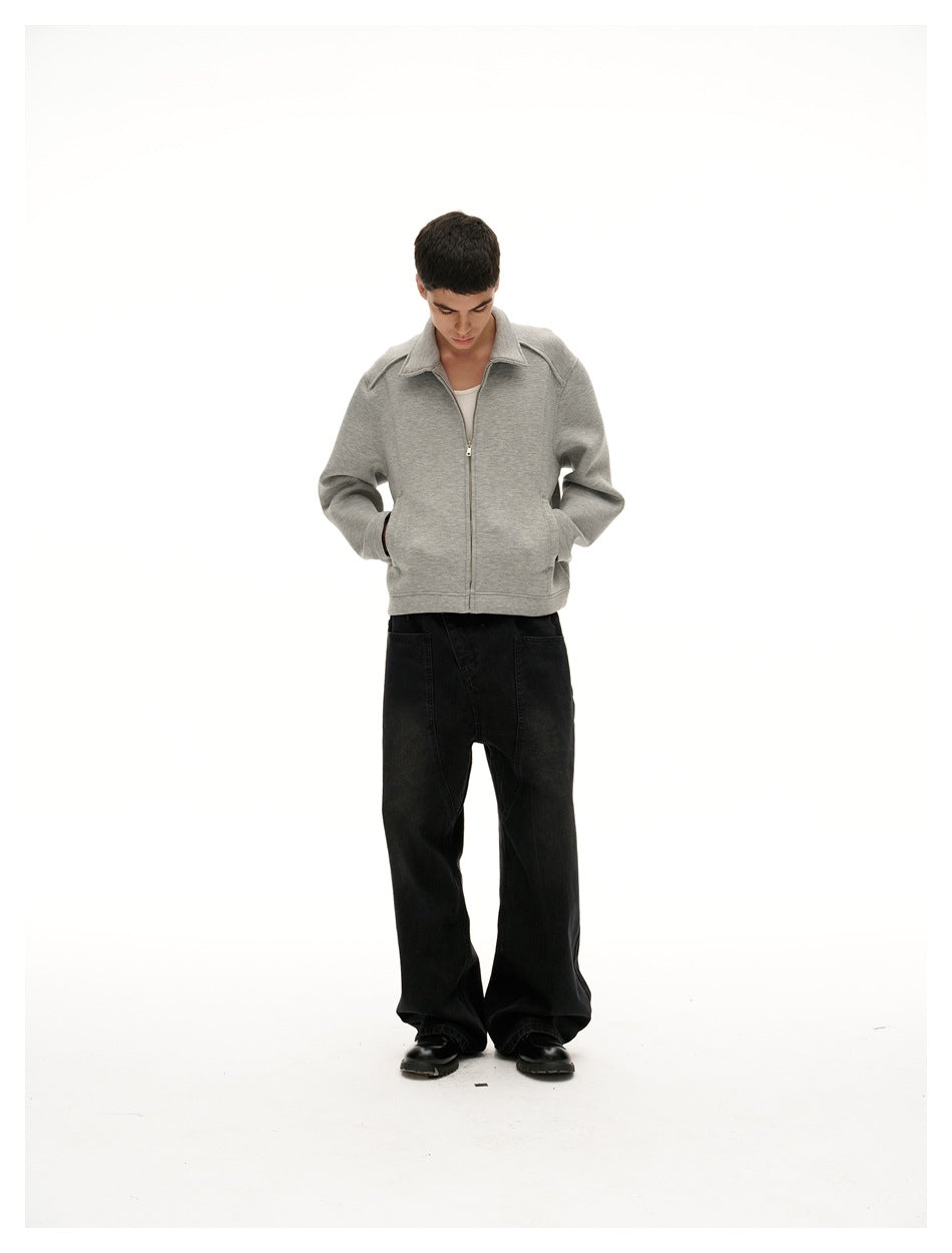 Model looking down with hands in pockets, wearing a light gray collared zip jacket and black wide-leg pants.