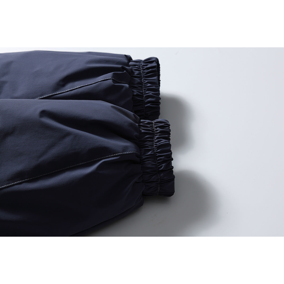 Close-up of two gathered elastic edges on the navy jacket fabric, showing the stitching and seams.