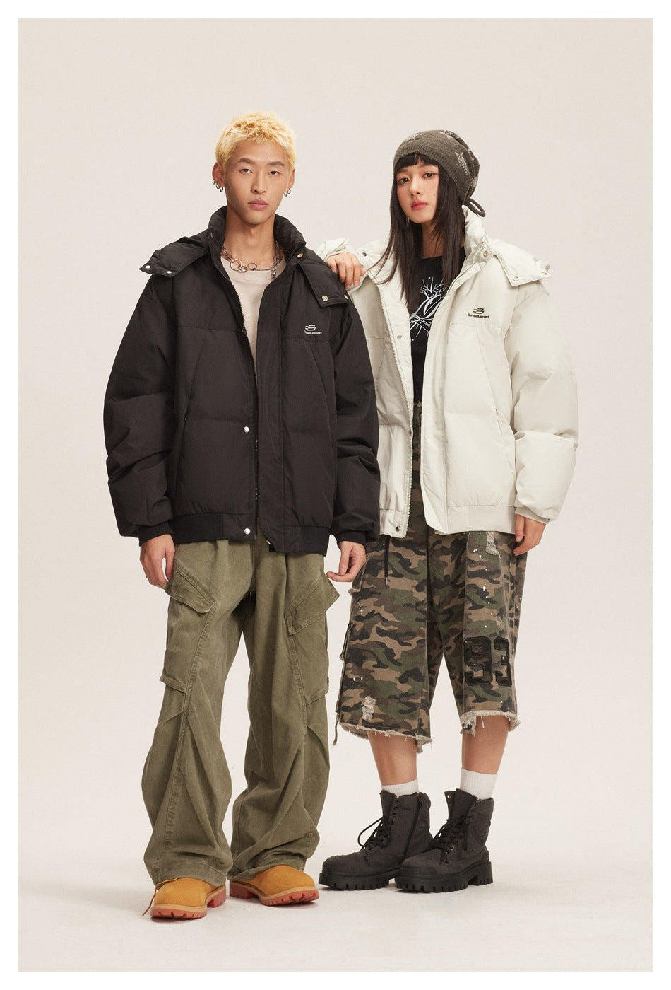 Two models wearing oversized puffer jackets in black and off-white with the hoods down, styled with cargo and camo bottoms