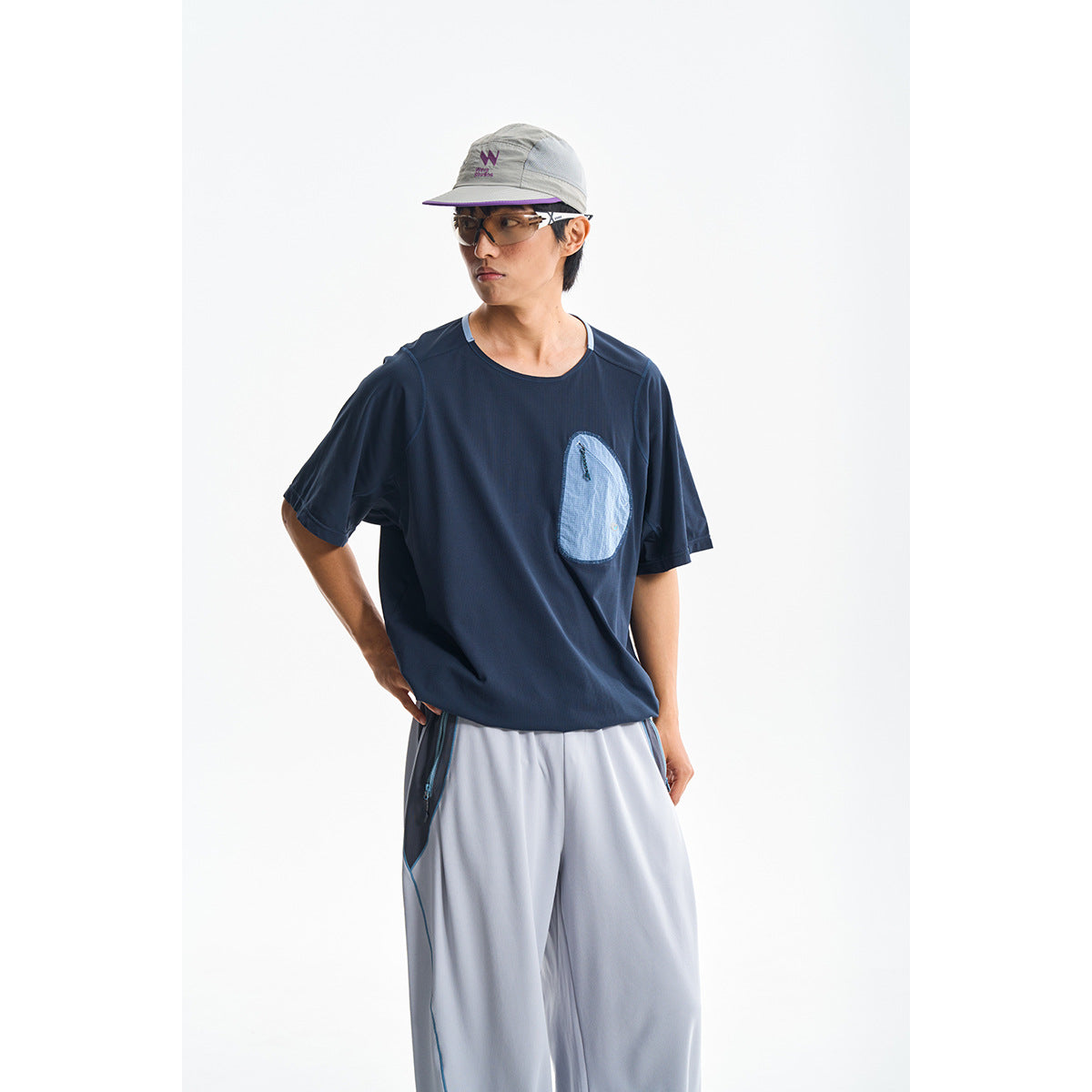 Model wearing a navy short-sleeve top with a light blue chest pocket and pale gray trousers.