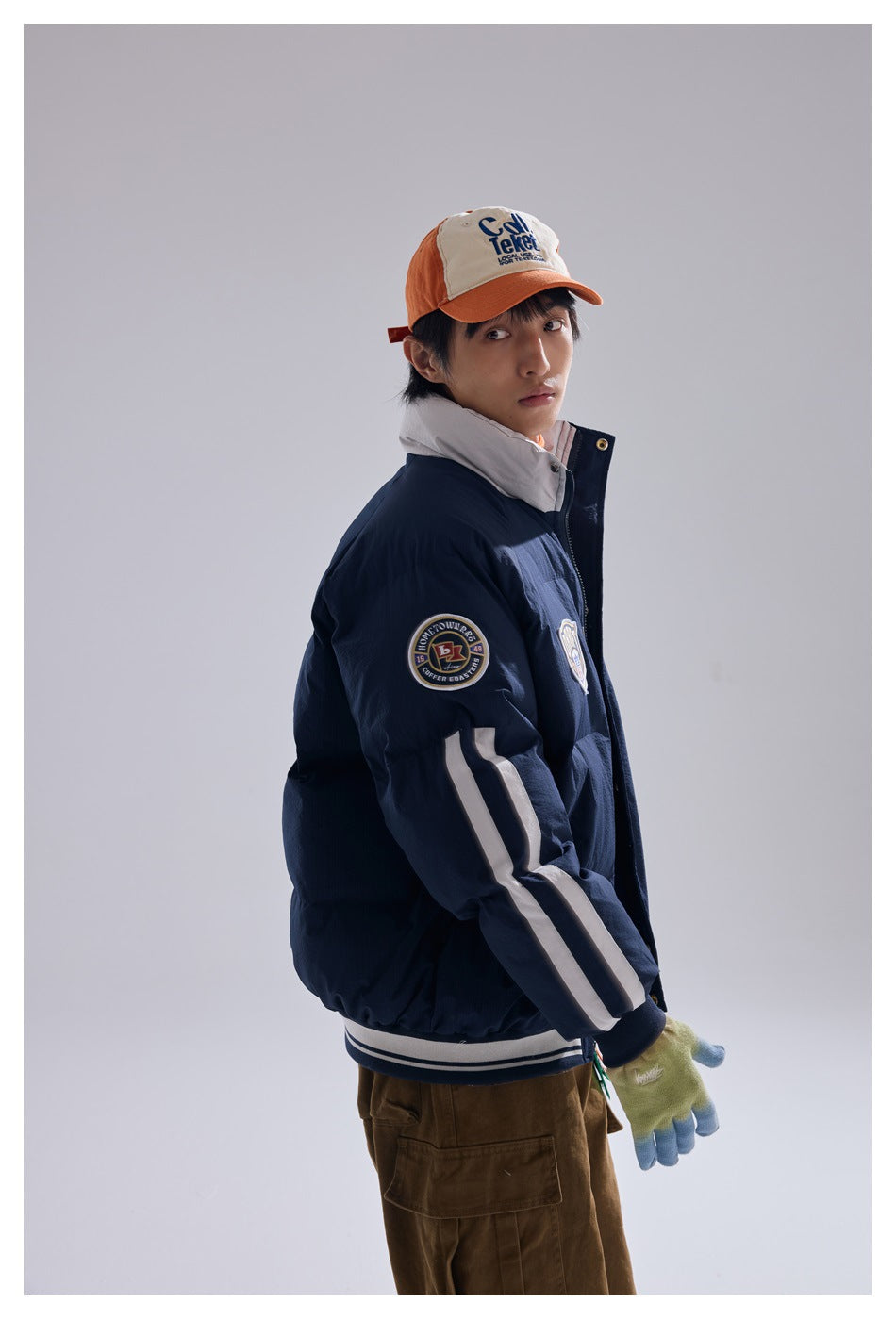 Model in a navy puffer jacket, shown at an angle with a sleeve patch, white sleeve stripes and ribbed hem.