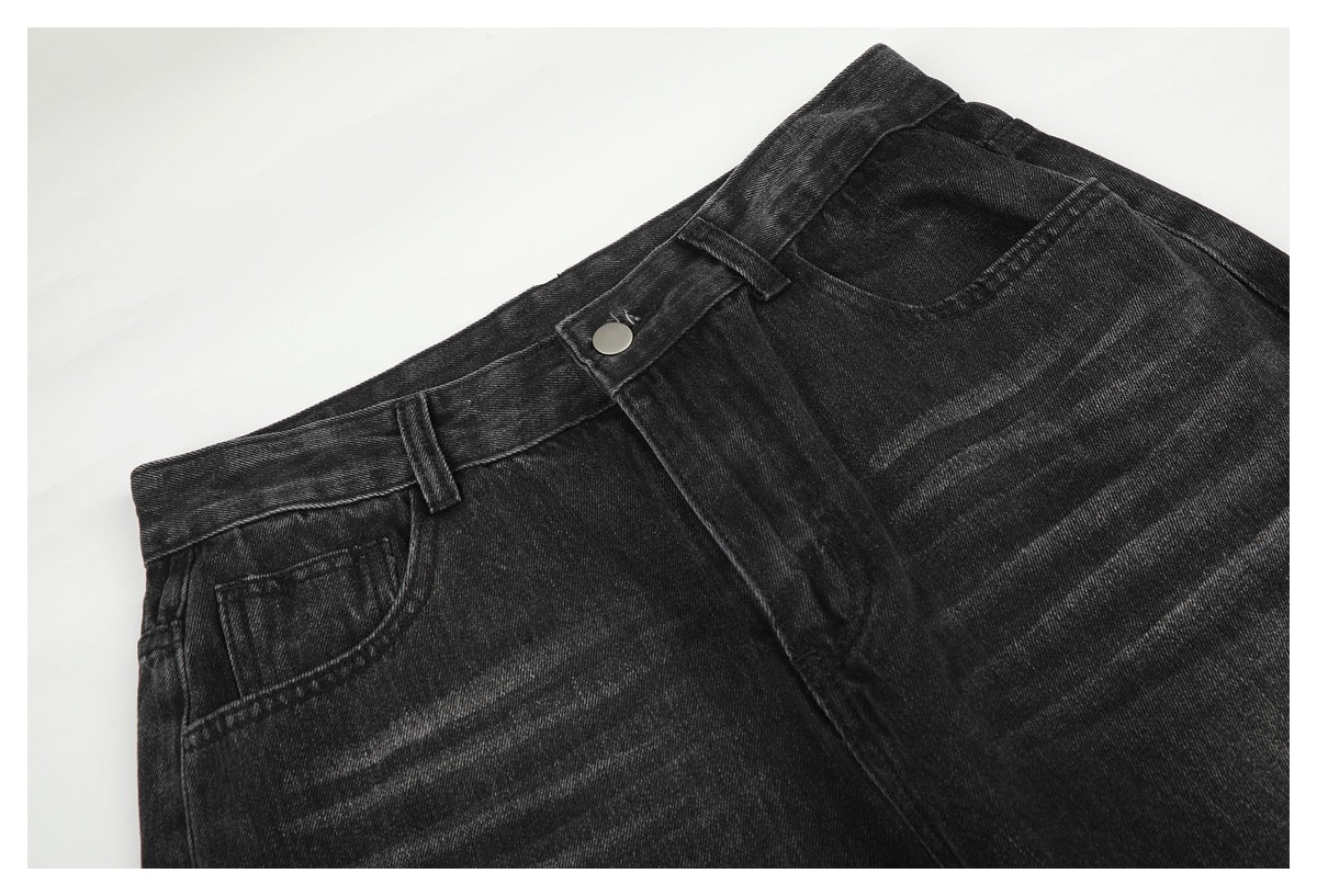 Angled close-up of the front waistband, button, belt loops and faded pocket area of charcoal-black jeans.