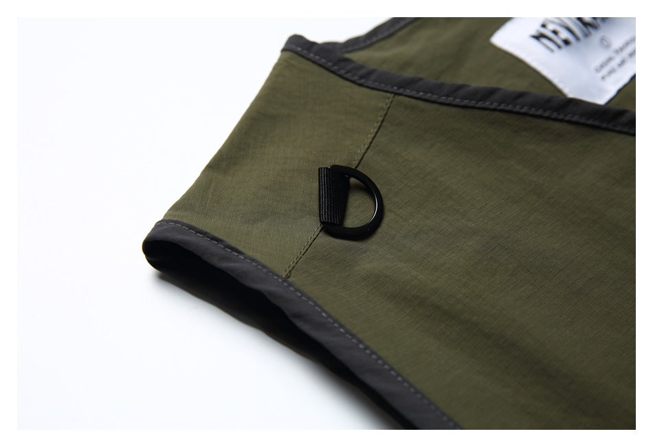 Close-up of the olive vest's dark-edged arm opening and black D-ring attachment.