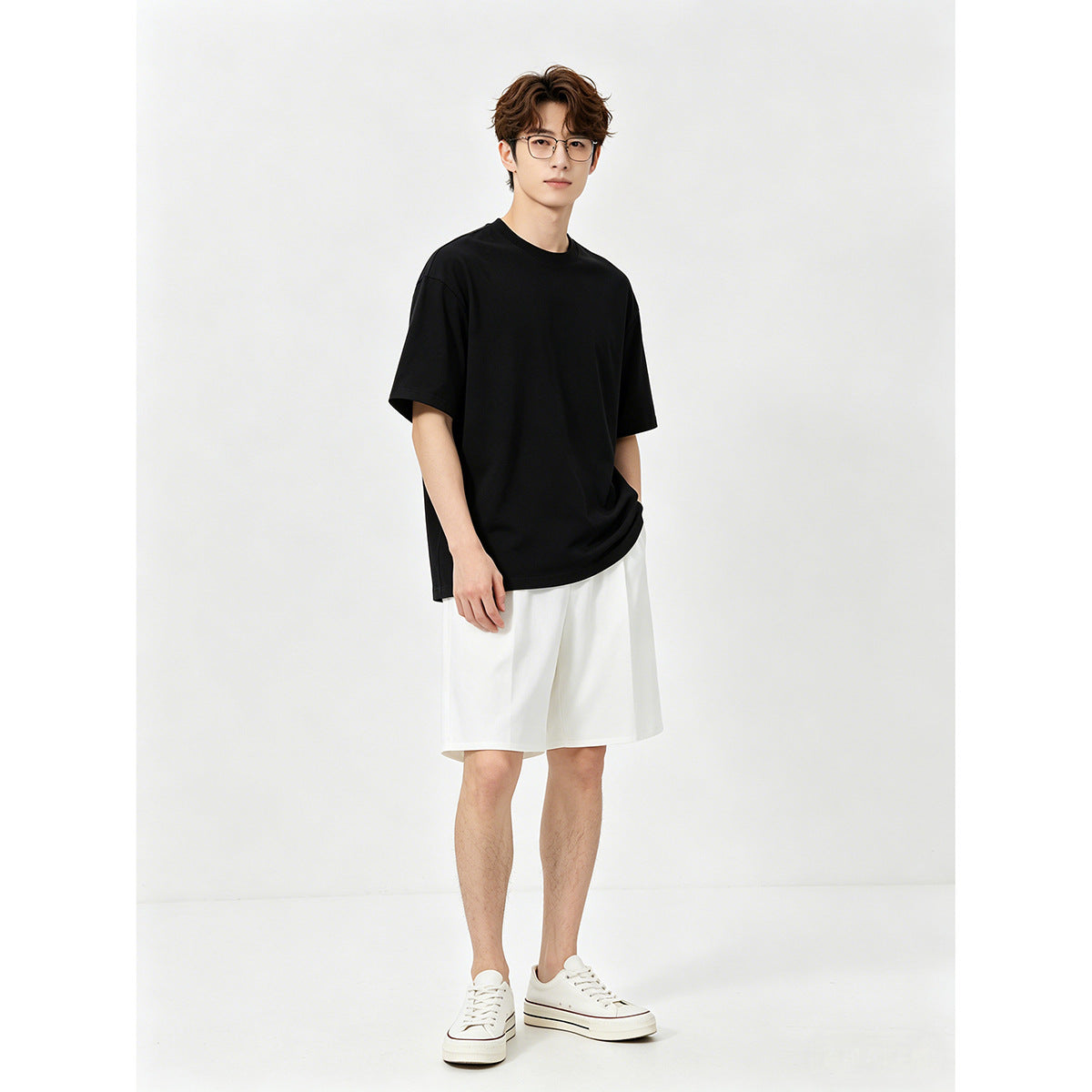 Model wearing a black crew-neck T-shirt, loose white shorts and white sneakers.