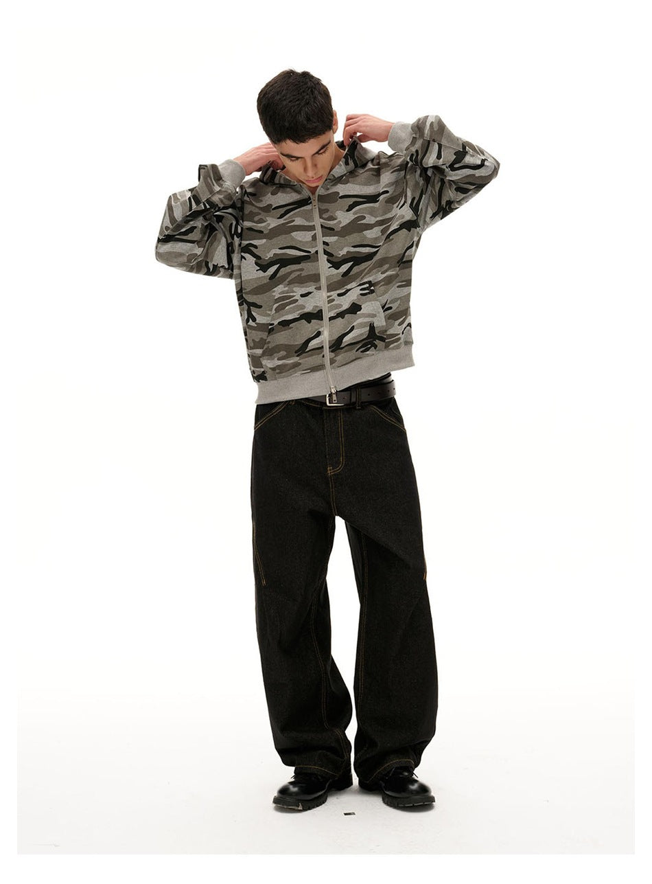 Model adjusting the hood of a gray camouflage zip-up hoodie, paired with loose black jeans.