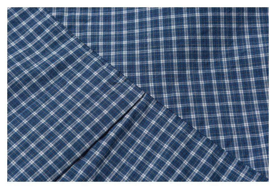 Close-up of blue plaid shirt fabric with overlapping folds and a visible stitched edge.