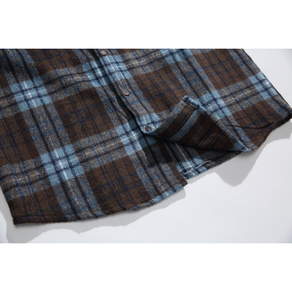 Close-up of the blue and brown plaid shirt hem, button placket, and sleeve cuff.
