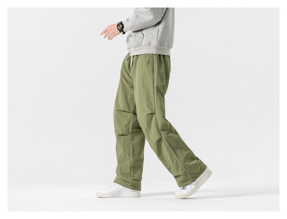Side view of a model walking in loose olive-green pants and white sneakers.