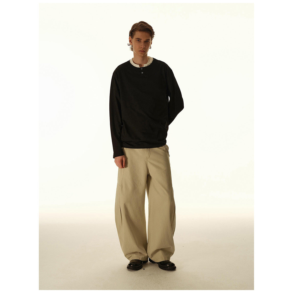 Full-length view of a model wearing a black long-sleeve henley and wide beige trousers.