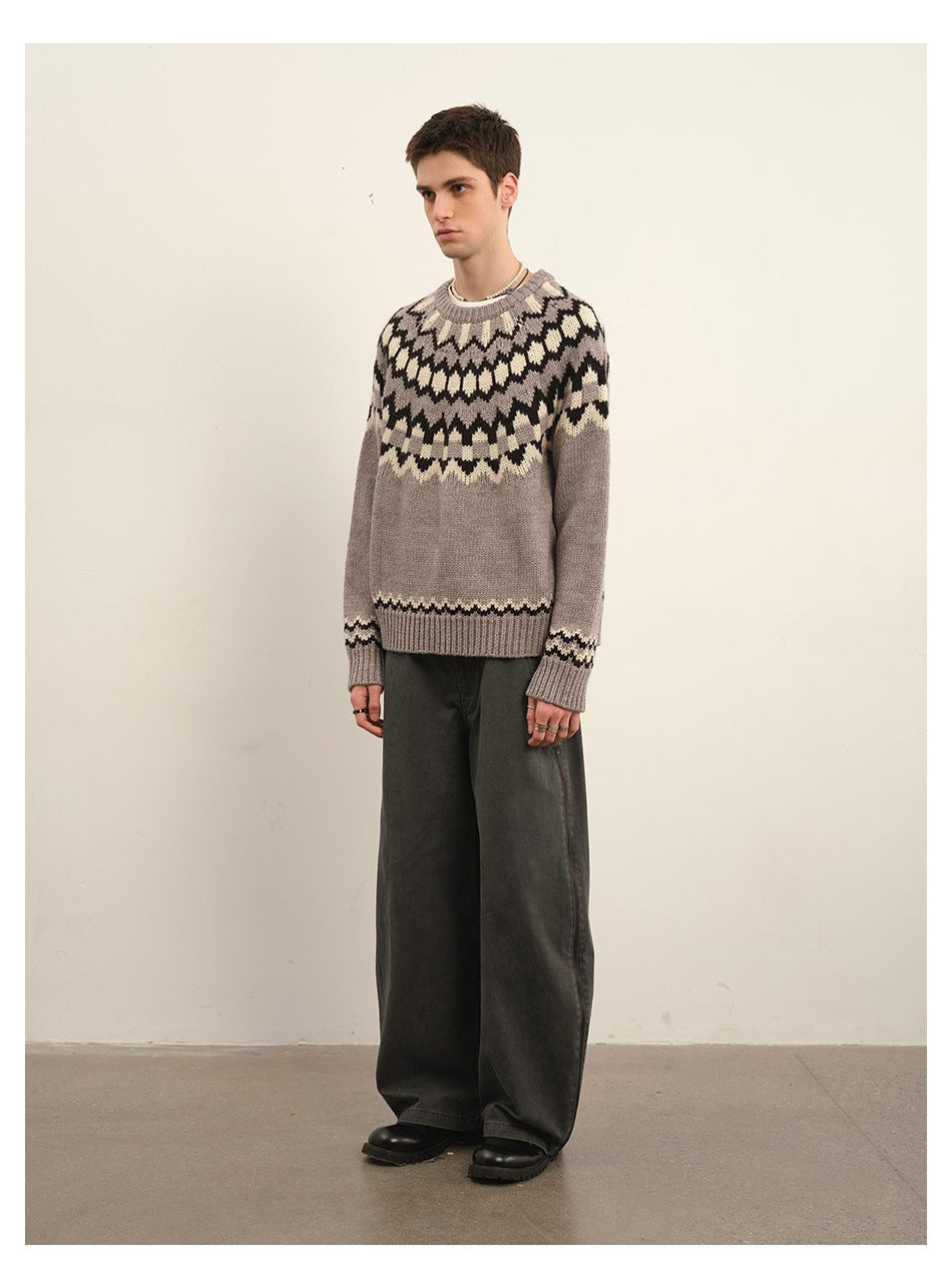 Model wearing a taupe Fair Isle crew-neck sweater with dark and cream patterns, paired with wide charcoal trousers.