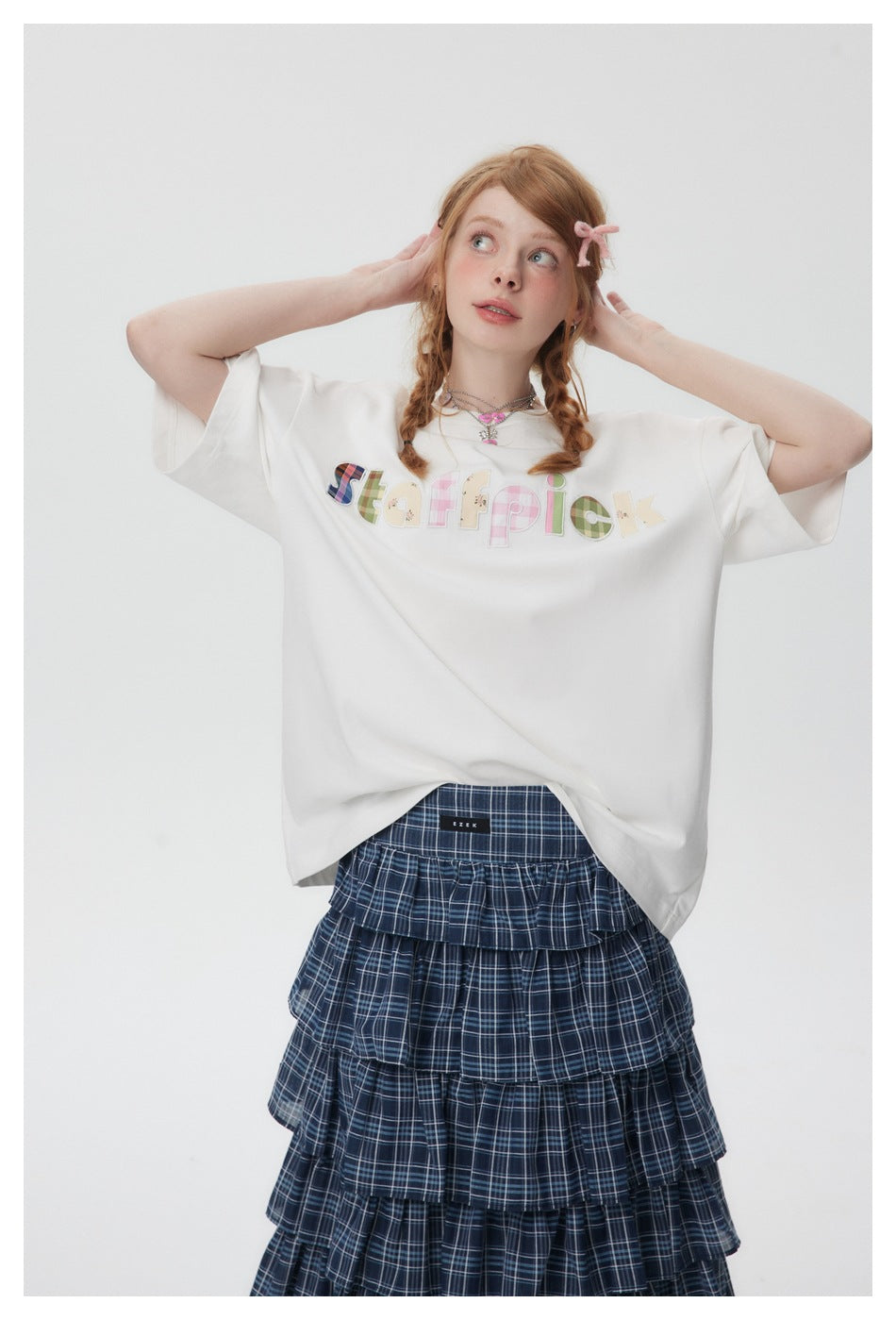Front view of a model wearing an oversized white T-shirt with colorful patchwork lettering and a navy plaid tiered skirt.