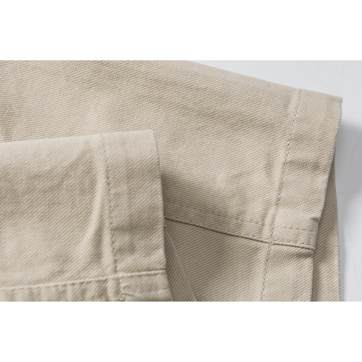 Close-up of beige shorts showing a stitched hem and overlapping fabric panels.