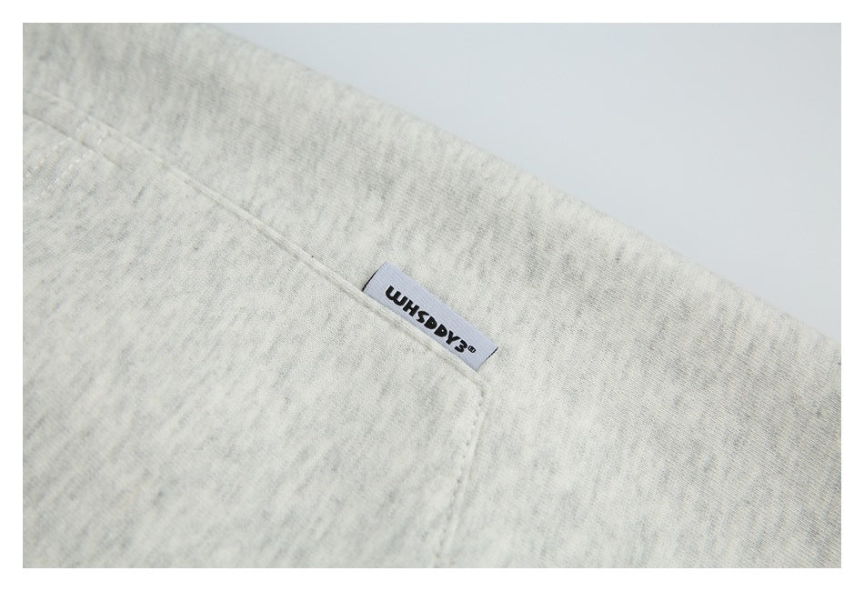 Close-up of a small woven English-text label at the edge of a rear pocket on light heather gray shorts.