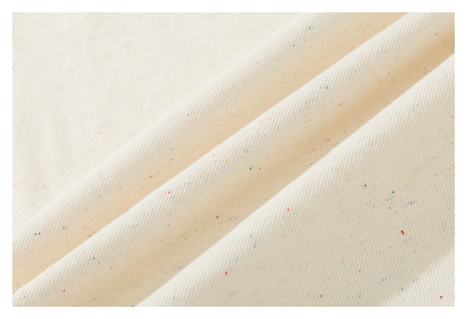 Close-up of off-white fabric with a fine weave and scattered multicolor flecks.