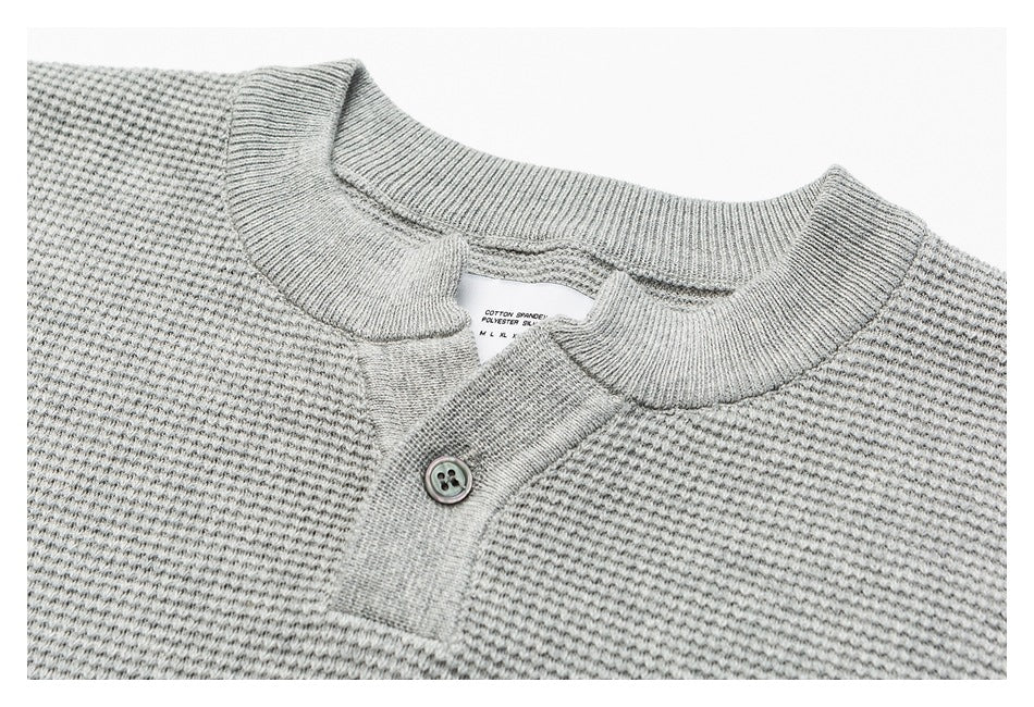 Close-up of a light gray knit sweater’s ribbed crew neck, button placket, and small inner care label.
