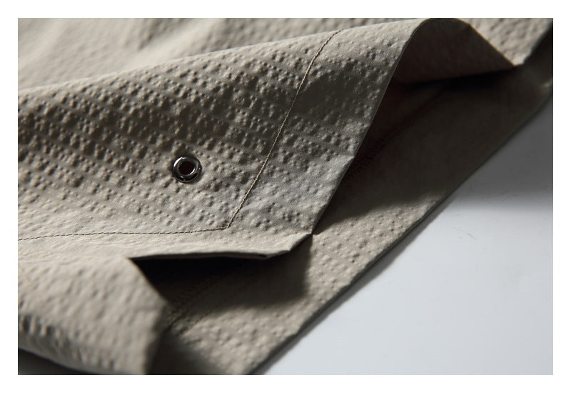 Close-up of a small metal eyelet on a stitched panel of taupe shorts.