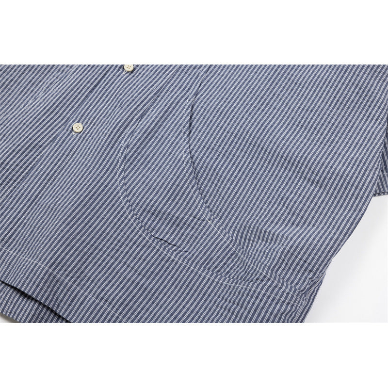 Close-up of a rounded chest pocket on a blue-gray shirt with fine white stripes.