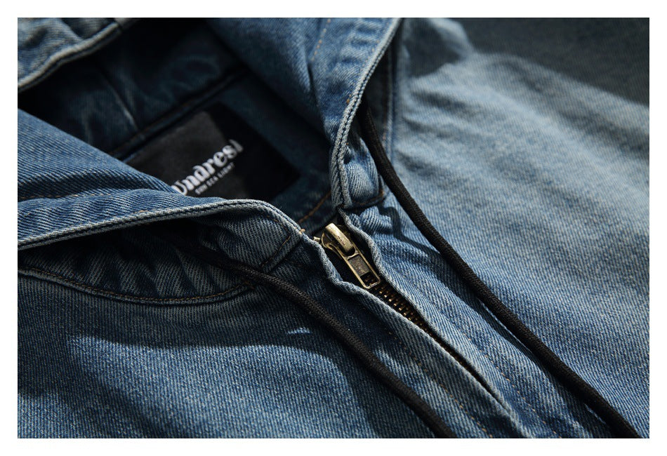 Close-up of a blue washed-denim jacket's brass zipper, black drawstring and sewn-in neck label.