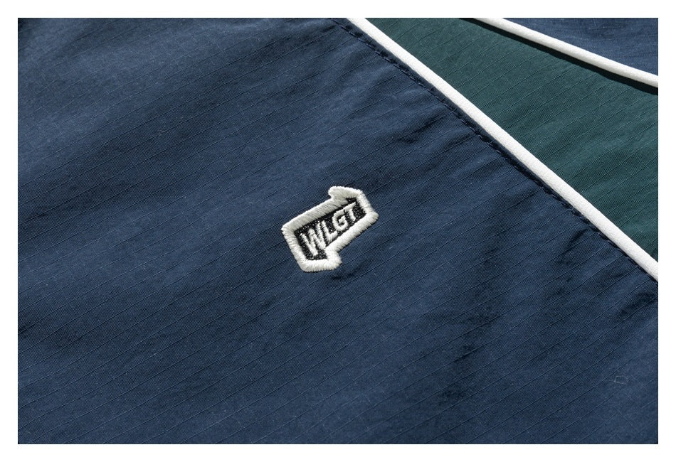 Close-up of a small embroidered patch on navy jacket fabric beside white piping and a dark green panel.