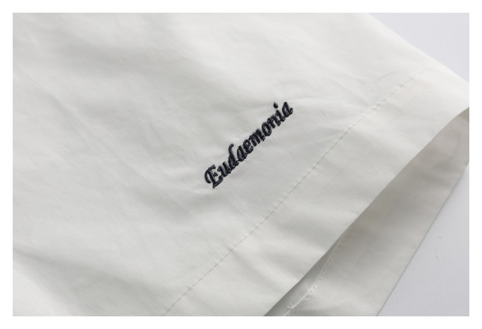 Close-up of dark script embroidery on white shirt fabric near a seam.