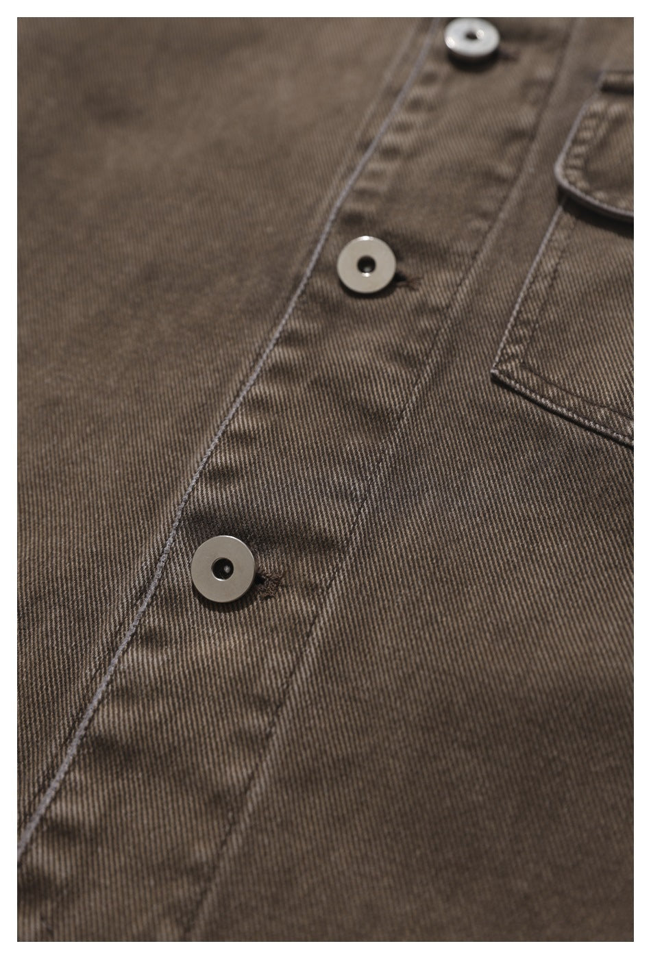 Close-up of the brown shirt's button placket, showing round buttons, stitching, and fine diagonal texture.